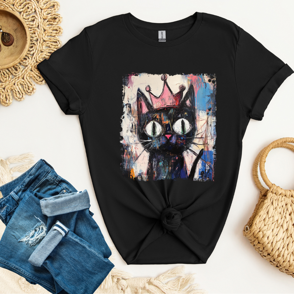 Black t-shirt with a colorful cat graphic on a white surface with denim shorts and a woven bag.