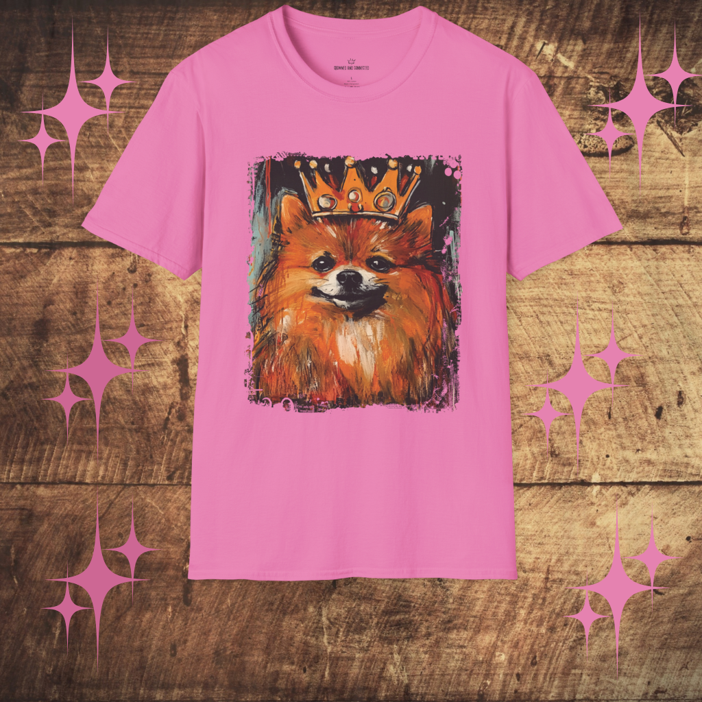 Pink t-shirt with a Pomeranian dog wearing a crown graphic on a wooden surface with decorative stars.