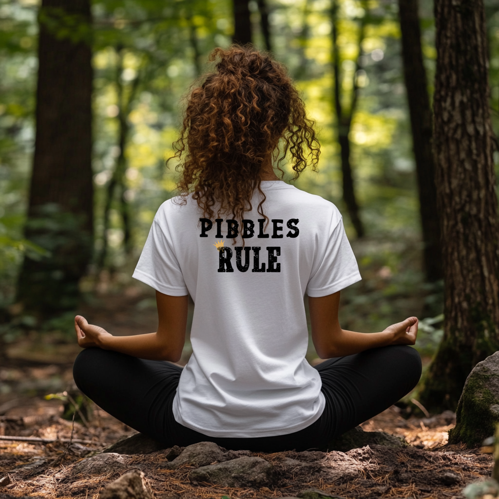 Person sitting in a meditative pose in a forest wearing a white t-shirt with 'PIBBLES RULE' text.