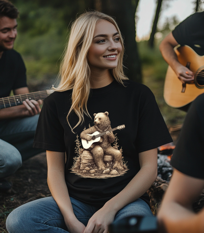 Ayoung blong girl sitting around a campfire with several people playing accoustic guitar. She is wearing a black Gildan 64000 t-shirt, with  a graphic of Van, The Grizzly Bear sitting on a stump playing an accoustic guitar.